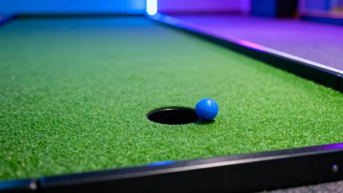 Indoor glow mini golf hole with green turf, black edging, a circular putting hole, and one blue ball
