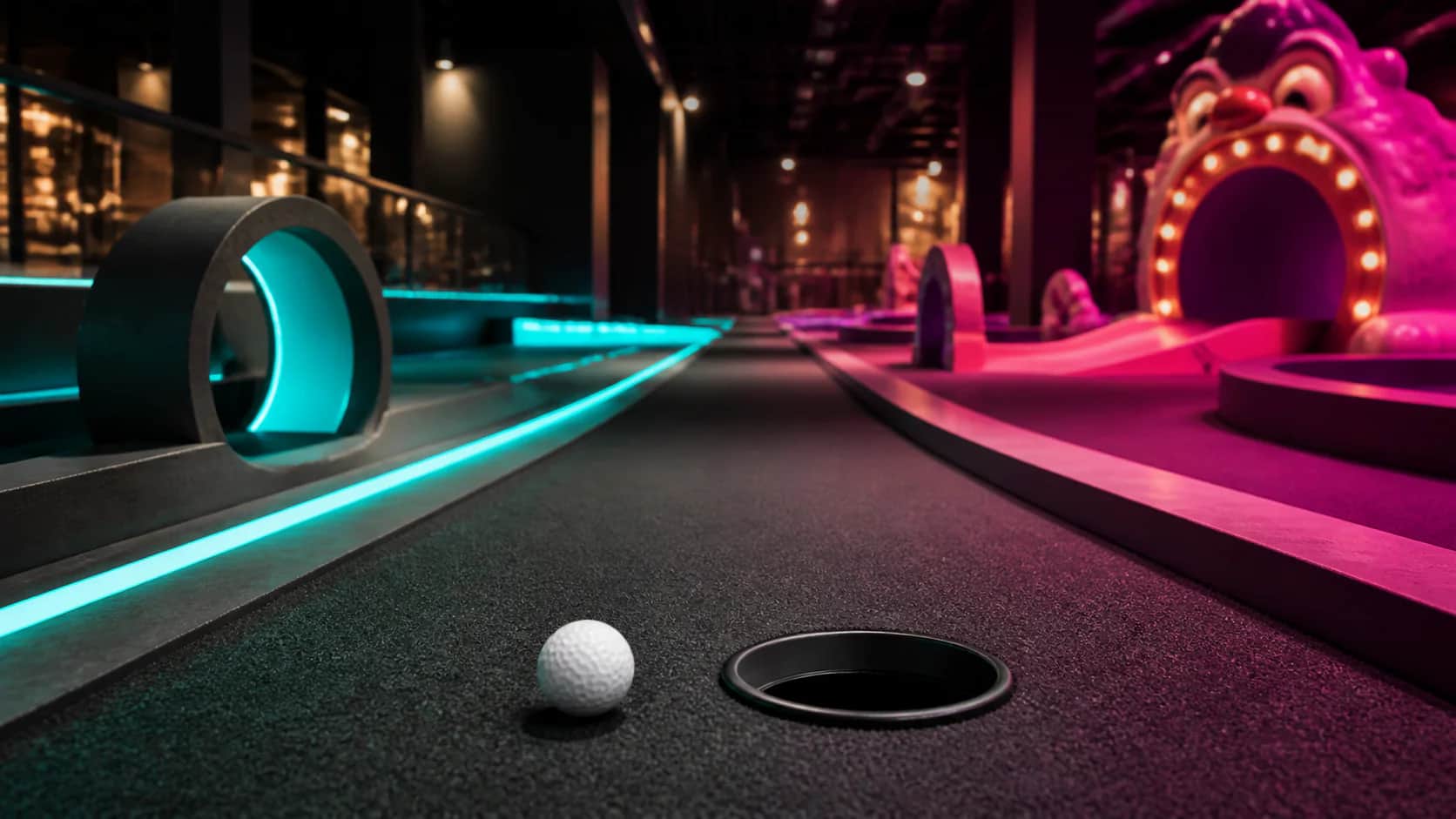 Indoor mini golf lane with split teal and magenta lighting, a circular black putting hole, and one yellow ball